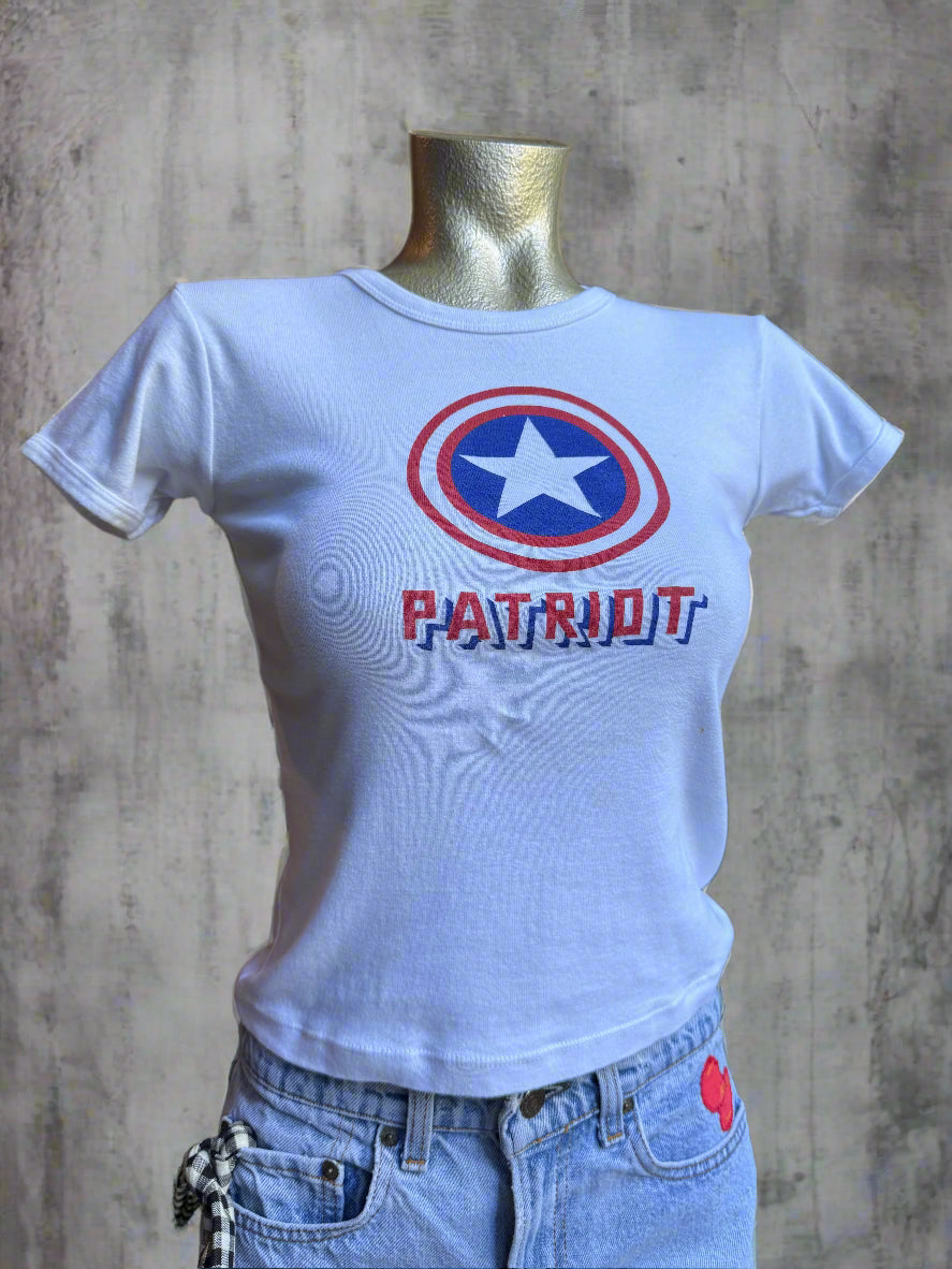 White t-shirt with a red, white, and blue design and text on a person wearing denim shorts.